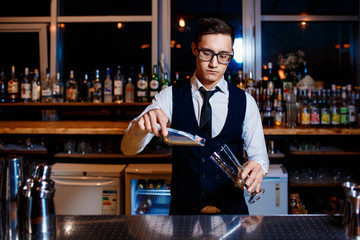 The bartender prepares a fresh, cold, alcoholic cocktail. Bar employee puts ice in his glass