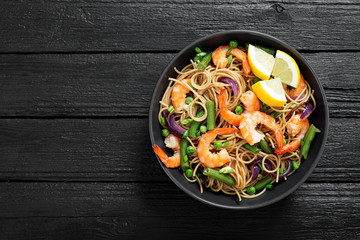 Stir fry noodles with shrimps and vegetables in black bowl.