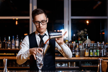 elegant young male barman prepares a delicious cocktail at the bar