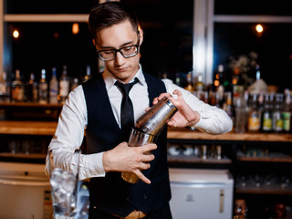 elegant young male barman prepares a delicious cocktail at the bar