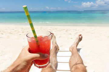 Man Lying On Deck Chair Holding Juice Glass At Beach