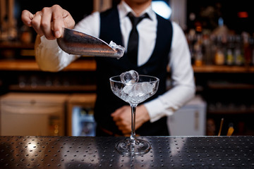 The bartender prepares a fresh, cold, alcoholic cocktail. Bar employee puts ice in his glass