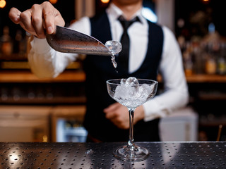 The bartender prepares a fresh, cold, alcoholic cocktail. Bar employee puts ice in his glass