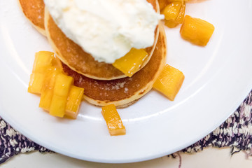 Breakfast pancakes on a plate with mango and sweet sauce.