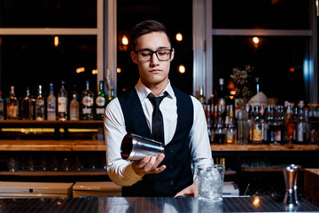 elegant young male barman prepares a delicious cocktail at the bar