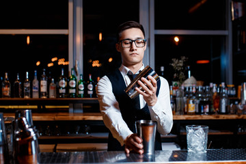 elegant young male barman prepares a delicious cocktail at the bar