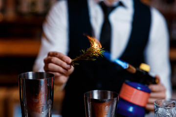 elegant young male bartender preparing a delicious cocktail at the bar. barman szmat razmarin gas torch