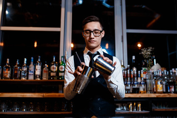 elegant young male barman prepares a delicious cocktail at the bar