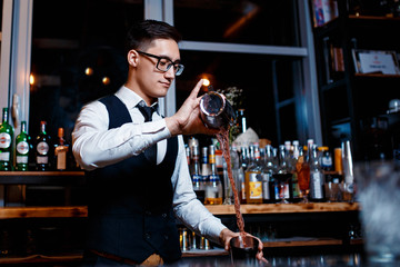 elegant young male bartender preparing a delicious cocktail at the bar. Bartender enjoys high cocktail