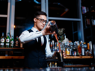 elegant young male bartender preparing a delicious cocktail at the bar. Bartender enjoys high cocktail