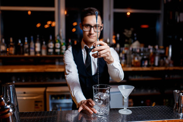 elegant young male barman prepares a delicious cocktail at the bar