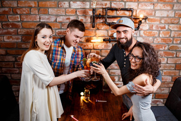 friends with smiles on their faces at the bar have fun, drink cocktails, cheks in glasses