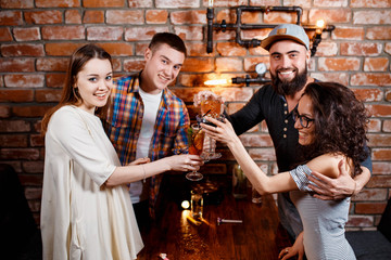 friends with smiles on their faces at the bar have fun, drink cocktails, cheks in glasses