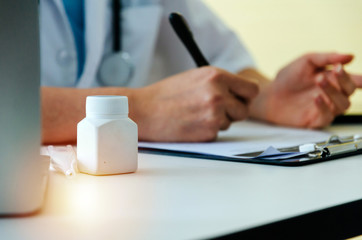 Fototapeta premium young man doctor or pharmacist with stethoscope writing prescription on clipboard and bottle of pills on desk with patient in hospital, health care, medical, medicine, pharmacy, insurance concept