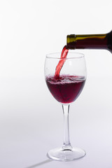 Fototapeta na wymiar Red wine pouring from bottle into big glass on white background