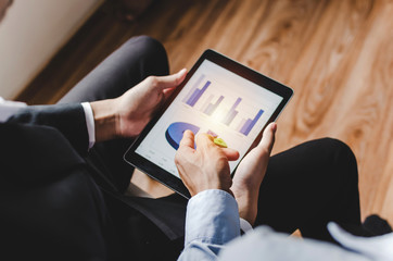two young partner business man investor talking and reading information about financial statistics chart in mobile tablet together sitting in office, finance, investment and digital technology concept
