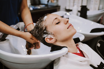 beauty and people concept - happy young woman with hairdresser washing head at hair salon