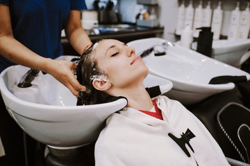 beauty and people concept - happy young woman with hairdresser washing head at hair salon