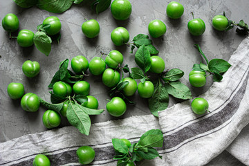 Green fresh organic plums on isolated background with blue and white cloth. On gray natural concrete background.