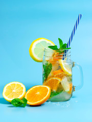 Infused detox water with ice, lemon and oranges slices with mint on blue background. Iced cold summer cocktail or lemonade in glass mason jar