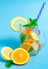 Infused detox water with ice, lemon and oranges slices with mint on blue background. Iced cold summer cocktail or lemonade in glass mason jar