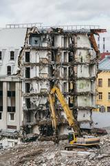 Yellow excavator with long mechanical arm makes a pause in the deamolition of the building. Vertical close up photo of destruction, power shovel, heavy machinery, bulldozer, excavator-destroyer.