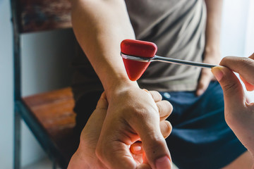 Doctor testing wrist joint reflex with red hummer jerk on young man.