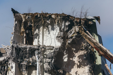 Photo of destroyed building, protruding reinforcement. Demolition of a building, house ruins, reconstruction, bricks and metal. Dismantling of structure.Heavy machinery, bulldozer, excavator-destroyer