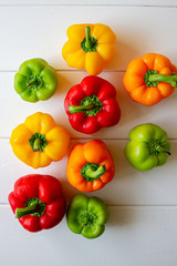 Green, orange, red and yellow fresh organic peppers on isolated background with blue and white cloth. On natural white wood background.
