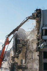 Excavator with long mechanical arm at height breaks off pieces of the house. Cleaning area for a new construction. Close up. Building demolition, destruction of a building, house ruins, reconstruction