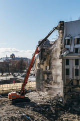 Vertical photo of excavator with long mechanical arm at height breaks off pieces of house. Cleaning area for a new construction. Building demolition, heavy machinery, bulldozer, excavator-destroyer.