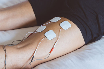 Patient applying electrical stimulation therapy on leg. Electrical tens.