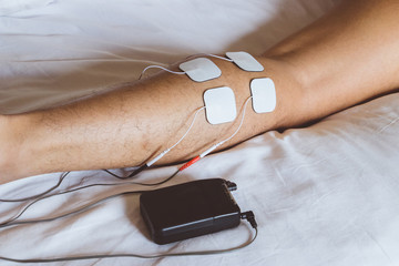 Patient applying electrical stimulation therapy on leg. Electrical tens.