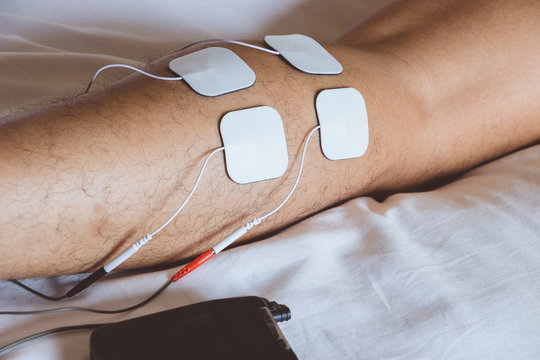 Patient Applying Electrical Stimulation Therapy On Leg. Electrical Tens.