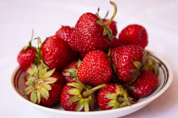 Beautiful, ripe red strawberries, shot from above in a ceramic saucer on a worn white background.