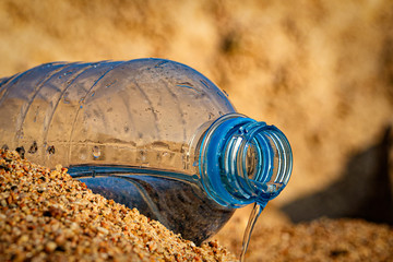 water flows out of a plastic bottle on the sea sand. water saving. last water drop