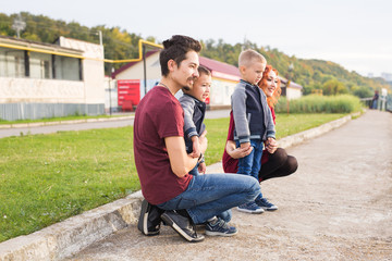 Fototapeta premium Parenthood, childhood and family concept - Parents and two male children walking at the park and looking on something