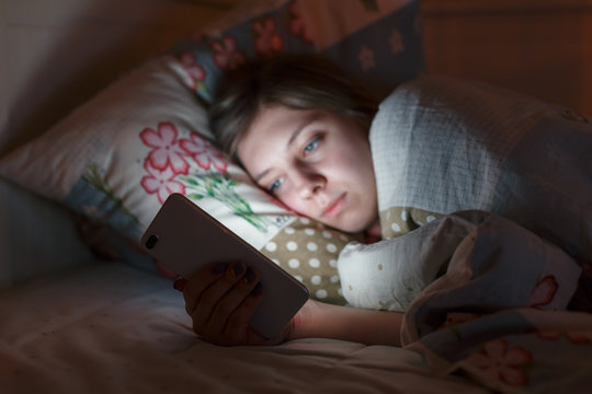 Young sleepy tired woman lying in bed using smartphone at late night, can not sleep. Selective focus. Social media addiction, loneliness, insomnia, nomophobia, sleep disorder, sleeplessness concept.
