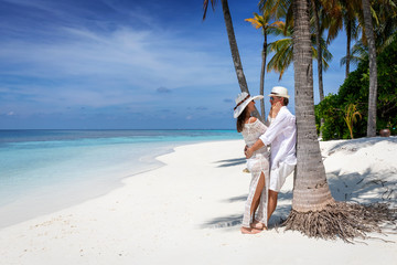 Attractive traveler couple in love enjoys their vacation time on a tropical beach with palm trees and turquoise ocean