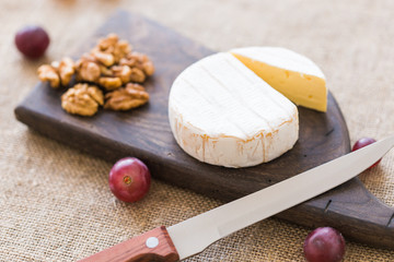 Brie type of cheese. Camembert cheese. Fresh Brie cheese on a wooden board with nuts and grapes....