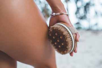 Young woman in tropical paradise is holding brush in hands antucellulite treatment. Cellulite...