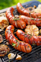 Grilled sausage with the addition of herbs and vegetables on the grill plate, close-up, outdoors. Grilling food, bbq, barbecue