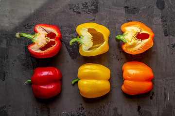 Green, orange, red and yellow fresh organic sliced peppers on isolated background with blue and white cloth. On gray natural concrete background.