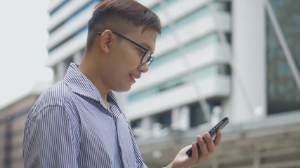 Slow motion portrait asian businessman answers the phone. Asian man with glasses use phone in street near big office building.