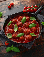 Homemade Meatballs in iron cast with sweet and hot tomato sauce, basil. On wooden table