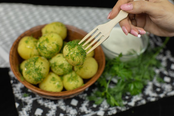 Woman's hand takes boiled new delicious potato using wooden fork