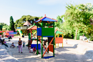 Unfocused photograph of an outdoor children's playground with children and families in it.