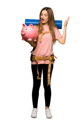 Full body Young backpacker woman surprised while holding a piggybank on isolated background