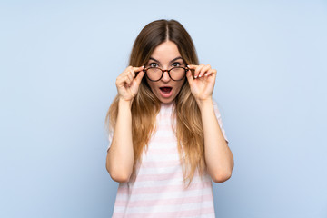 Young woman over isolated blue background with glasses and surprised