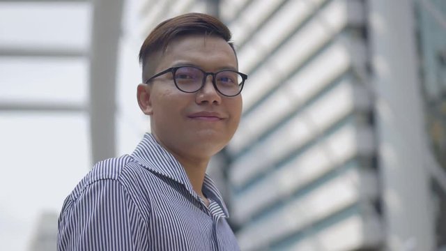 Slow motion portrait asian businessman smiling and looking at camera standing on urban city.